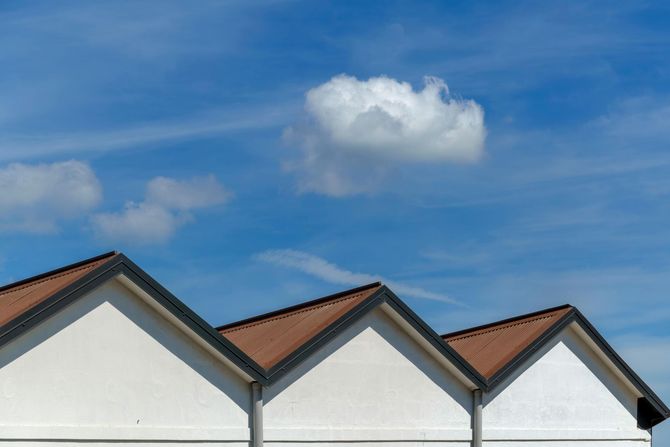 Three white, triangular gables with brown roofs against a vibrant blue sky with scattered white clouds.