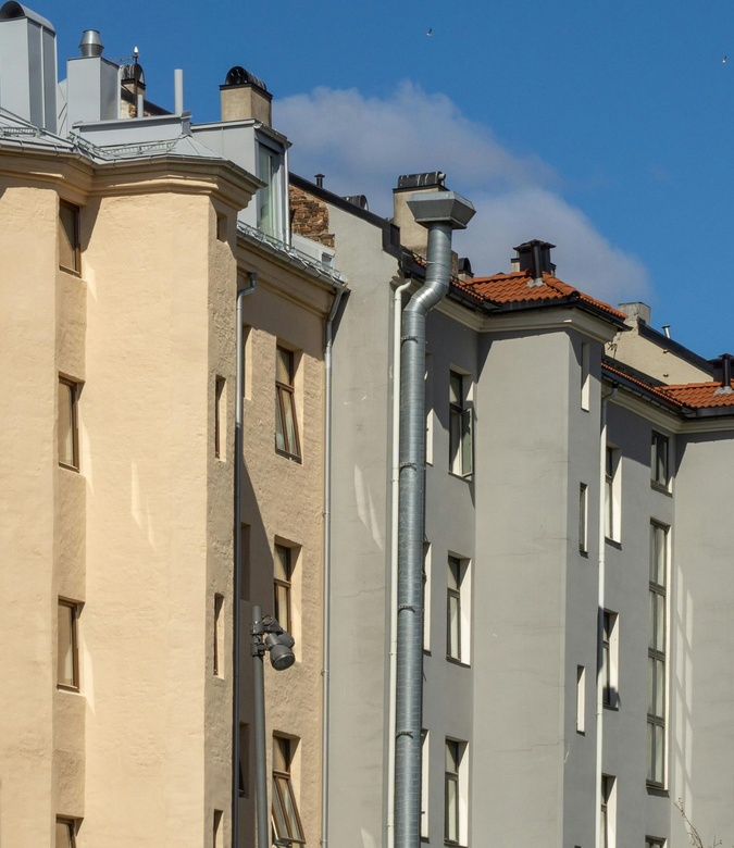 A view of two adjacent buildings in cream and light grey with metal downspouts and tiled rooftops against a blue sky.