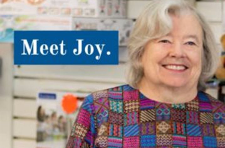 A woman is smiling in front of a sign that says meet joy