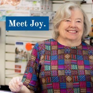 A woman is smiling in front of a sign that says meet joy