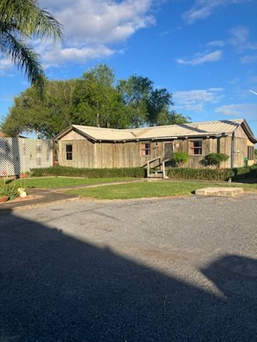 A large wooden house with a white roof is sitting on top of a lush green field.