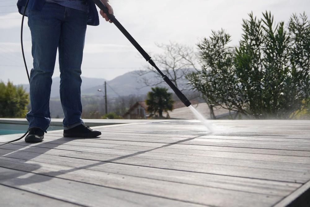 A person is using a high pressure washer to clean a wooden deck.