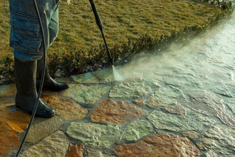 A man is using a high pressure washer to clean a stone walkway.