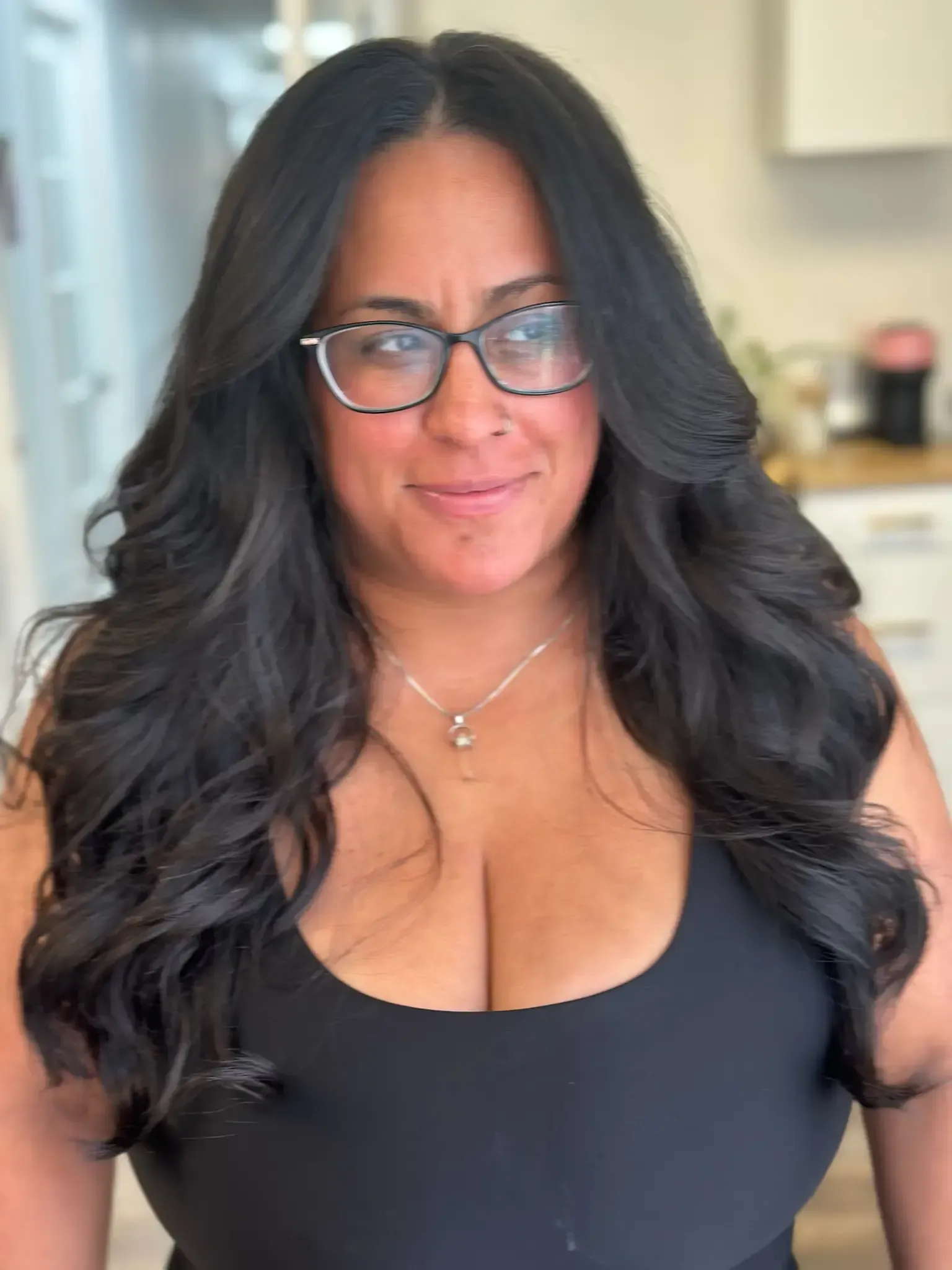 Woman with long, wavy black hair wearing glasses and a black tank top, smiling.