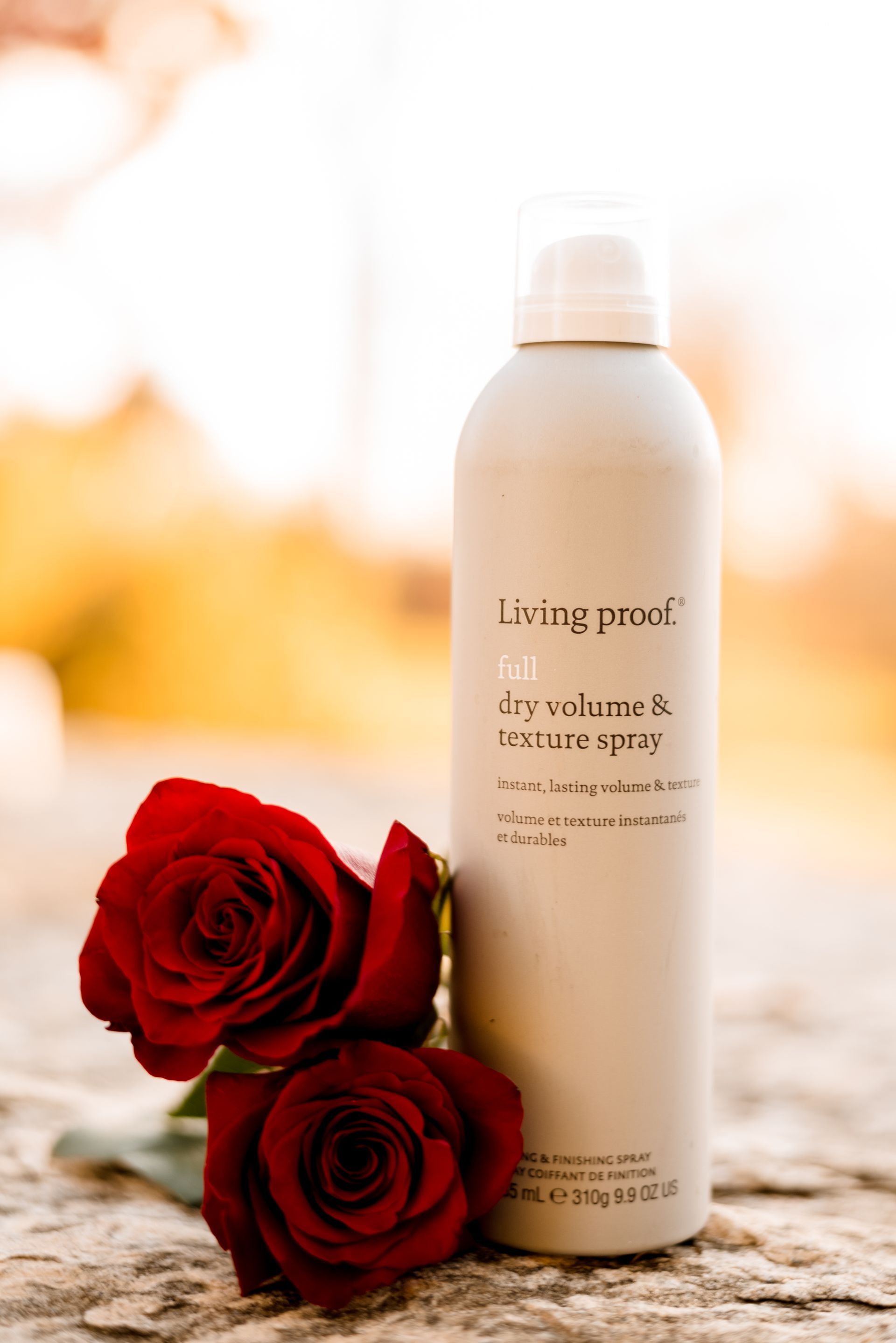 Bottle of Living Proof dry volume and texture spray next to two red roses on a stone surface.