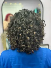 Dark curly hair in a bob style, viewed from the back. The person is wearing a blue top, and a mirror is behind them.
