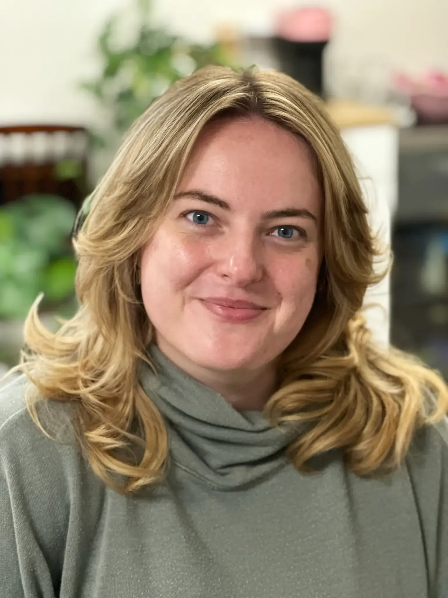Woman with blonde hair, smiling, wearing a green sweater.