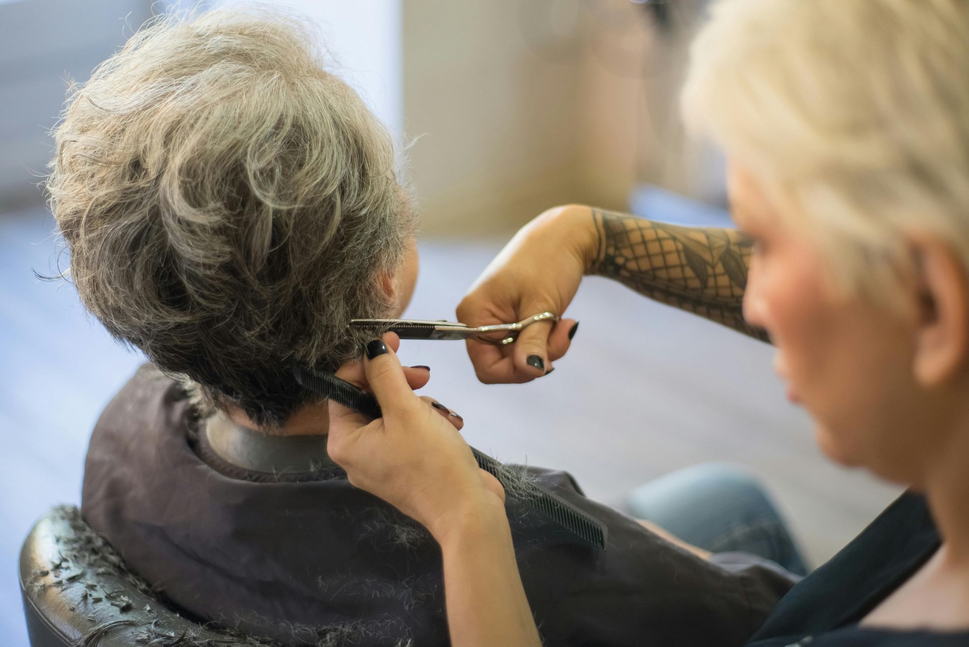 Hair stylist cutting a client's gray hair with scissors in a salon.