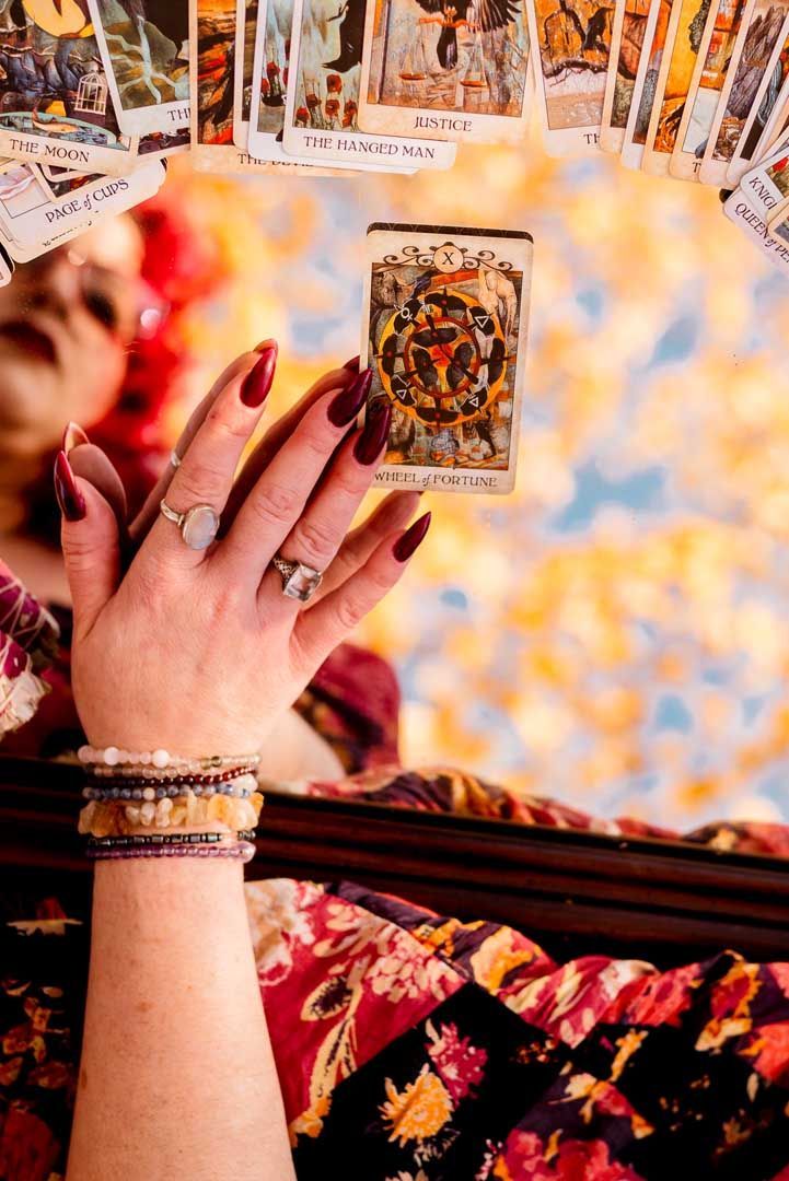 Hand holding a tarot card with a colorful background; other cards are in view.