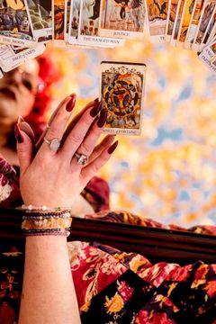 Hand holding a tarot card with a colorful background; other cards are in view.