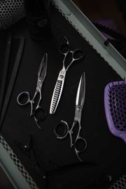 Hairdressing tools: scissors, combs, and brush on a dark surface, top-down view.