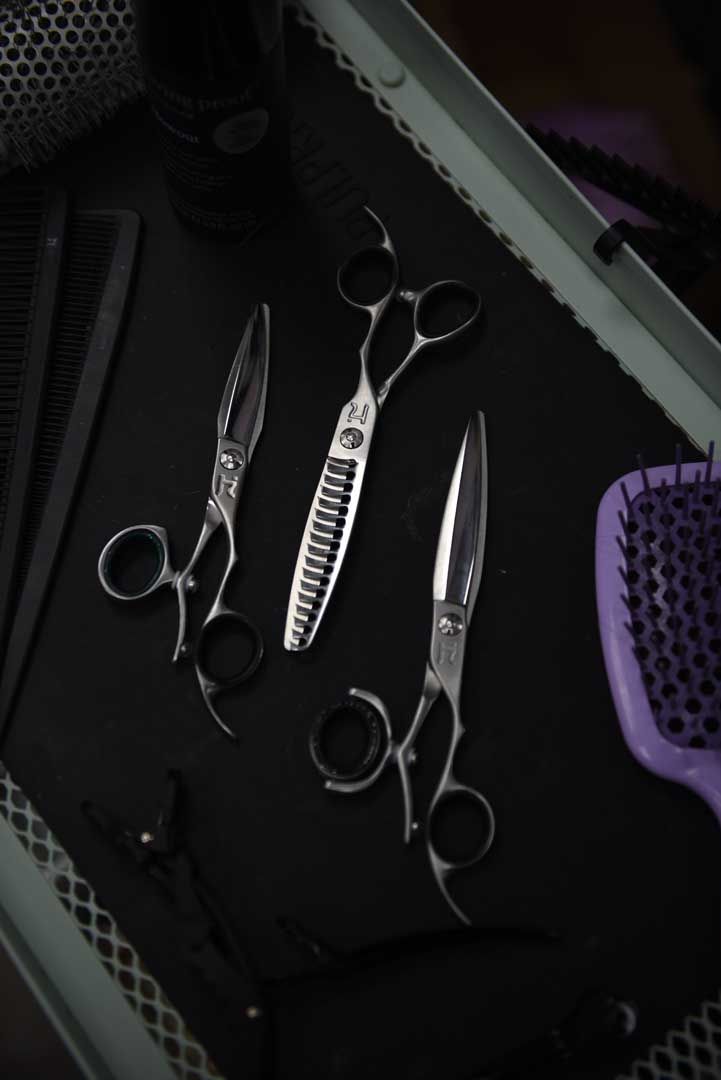 Hairdressing tools: scissors, combs, and brush on a dark surface, top-down view.