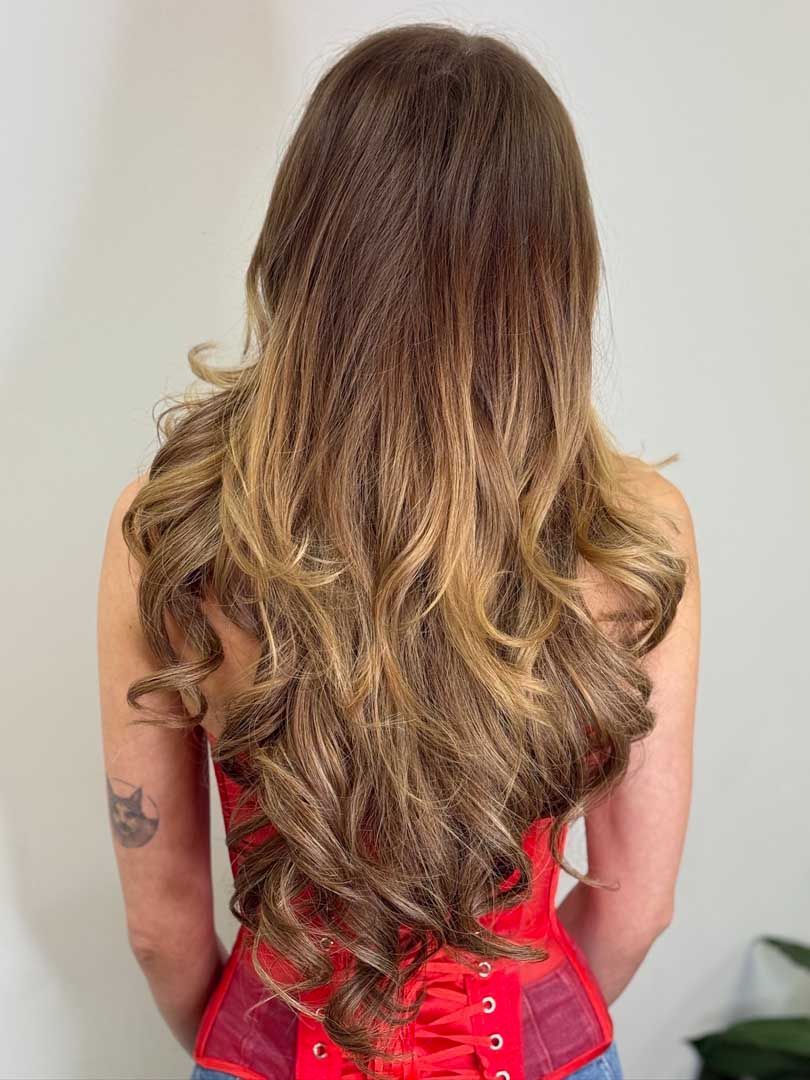 Woman with long wavy brown hair wearing a red corset, back view.