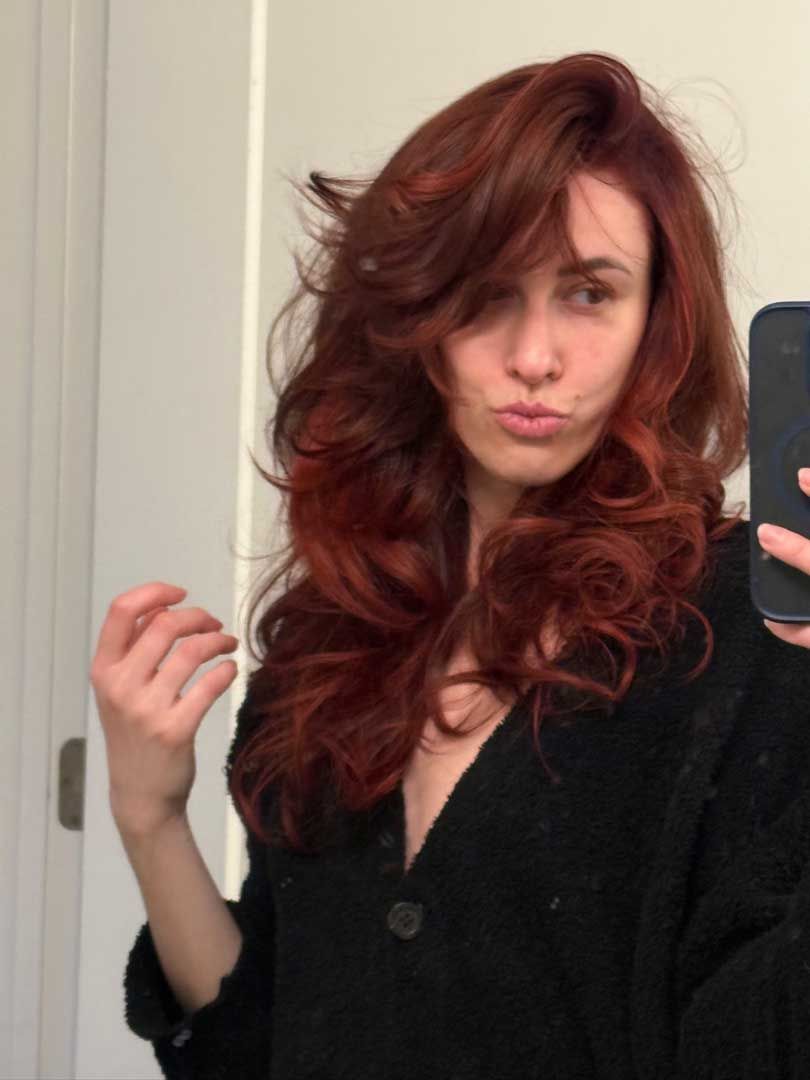 Woman with auburn hair, pouting and holding a phone, in a bathroom.
