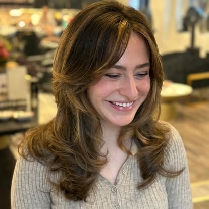 Woman with layered brown hair, smiling, wearing a beige sweater.