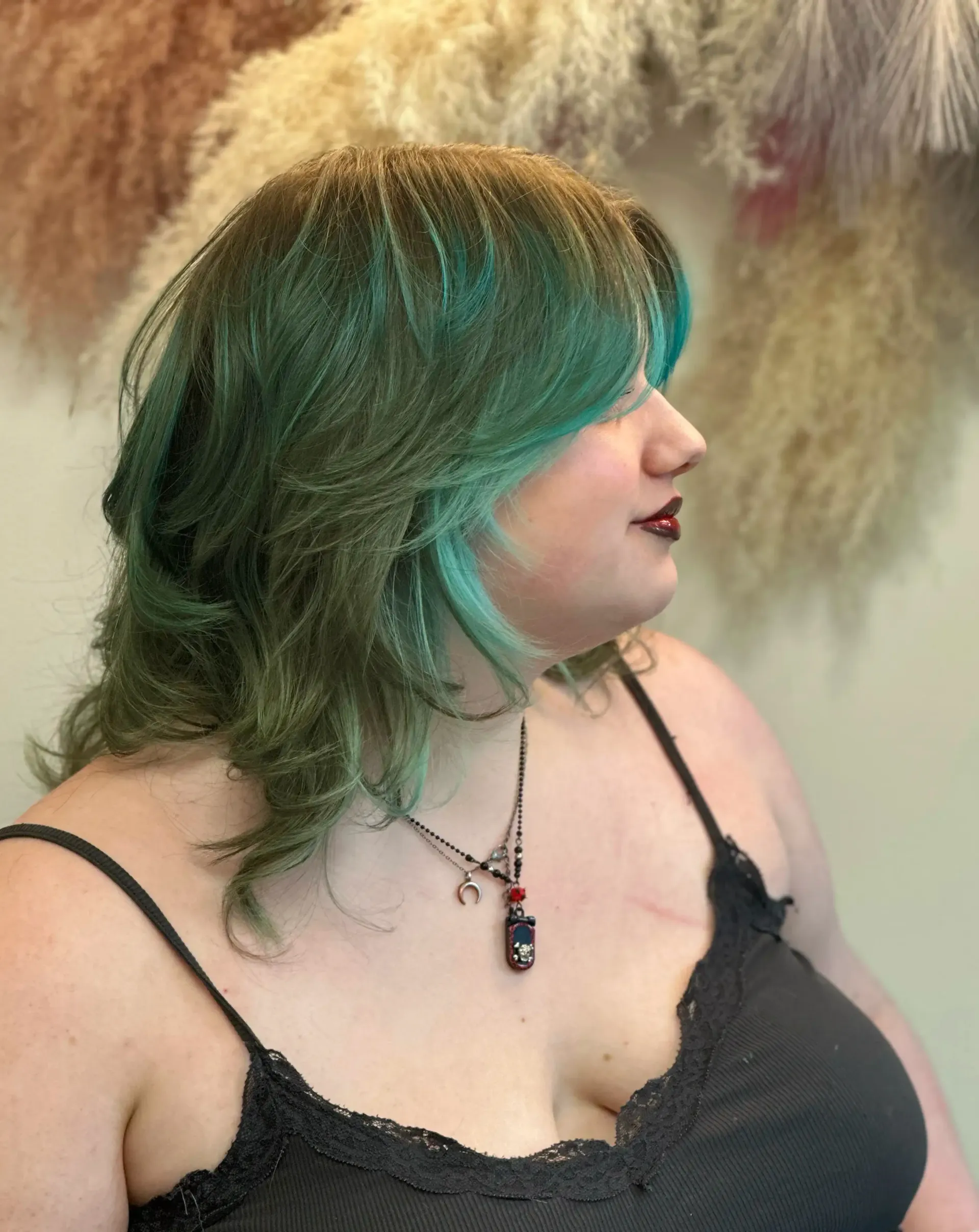Woman with green layered hair, wearing black camisole and necklace, looking to the side.