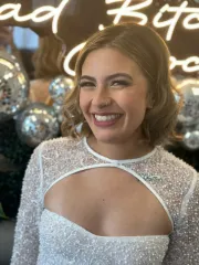 Woman in white sequined dress smiles; disco ball backdrop.
