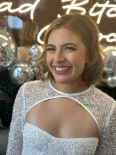 Woman in sparkly white dress, smiling.  Background includes silver disco balls and neon sign.
