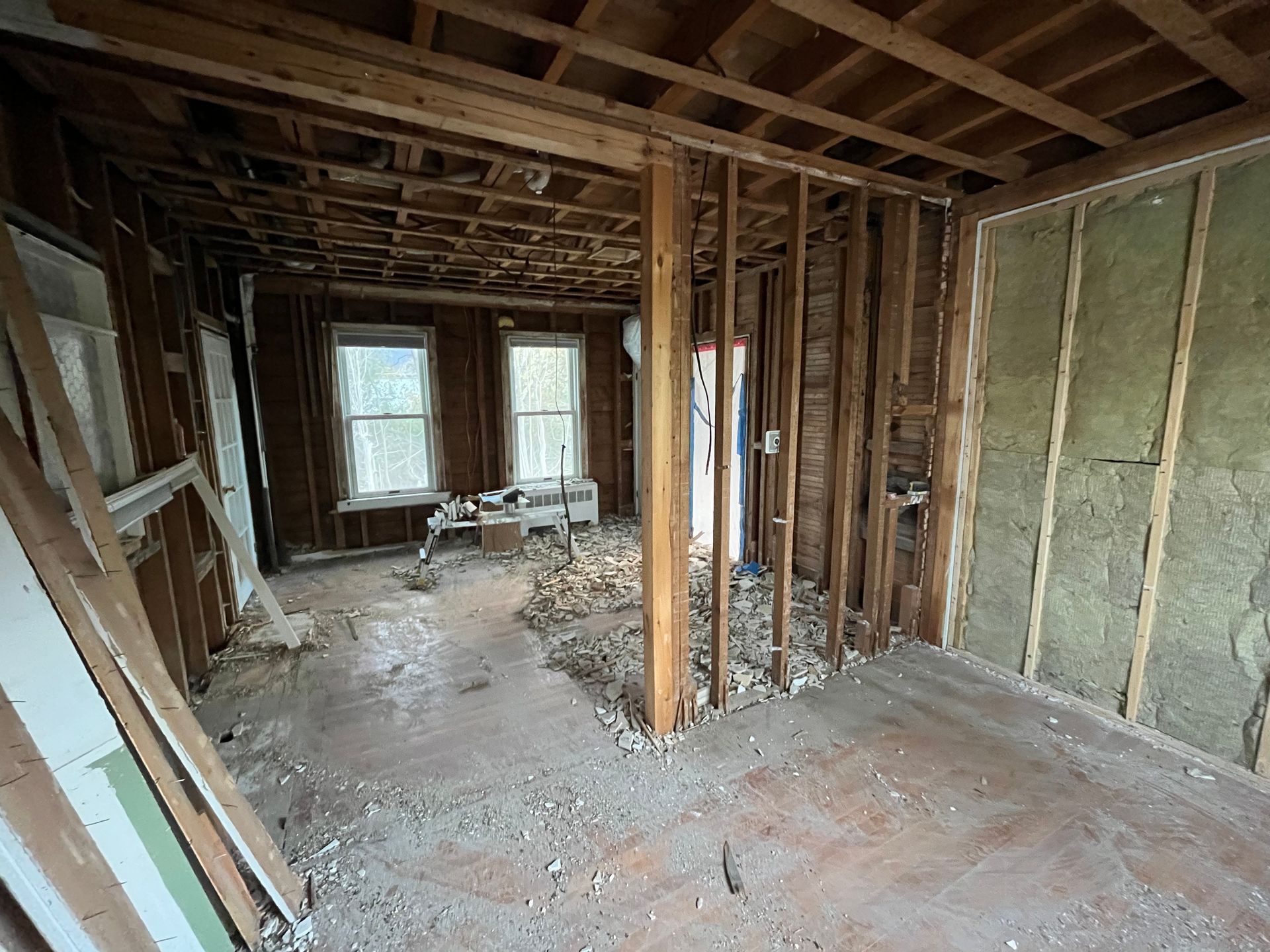 Interior view of a residential room during renovation with exposed wall studs, joists, and fiberglass insulation.