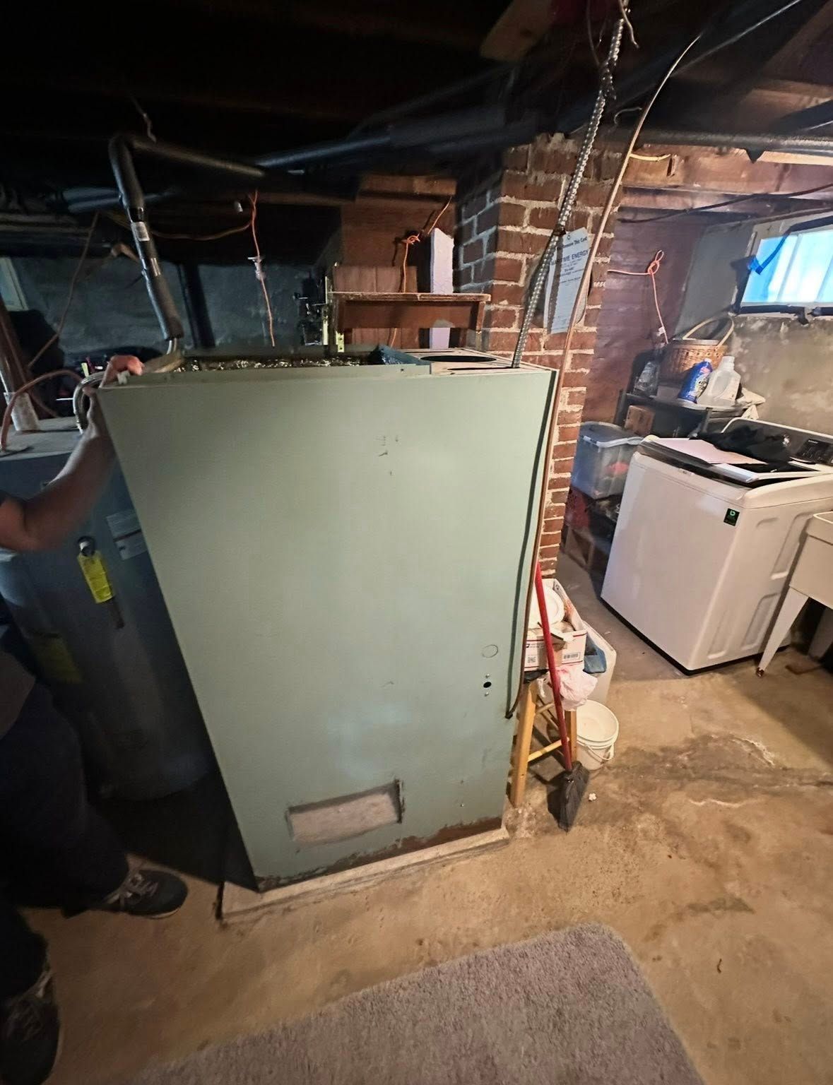 A light green HVAC unit stands in a dimly lit basement next to a water heater and a white washing machine.
