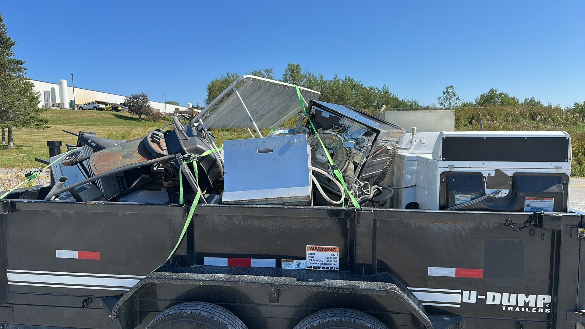 A U-Dump trailer filled with various metal scrap items and appliances under a clear blue sky.