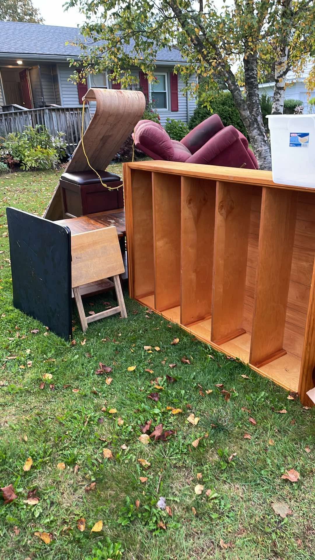 An assortment of used furniture, including a wooden bookshelf, a black tabletop, and cushions, sitting on a grassy lawn.