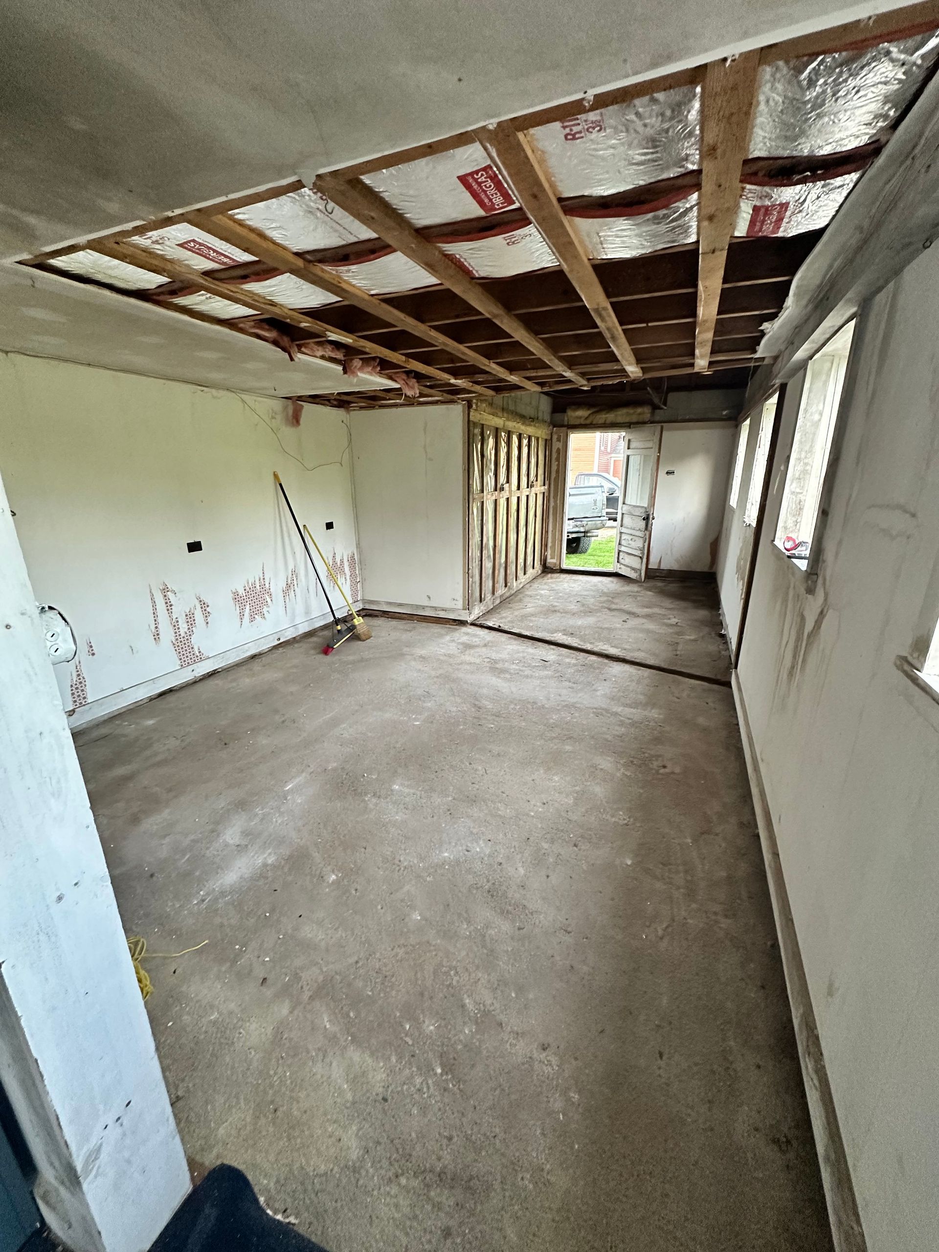 An interior view of a room under construction, featuring exposed ceiling rafters with insulation and a concrete floor.