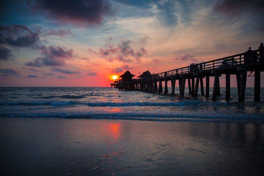 The sun is setting over the ocean and a pier is in the foreground.