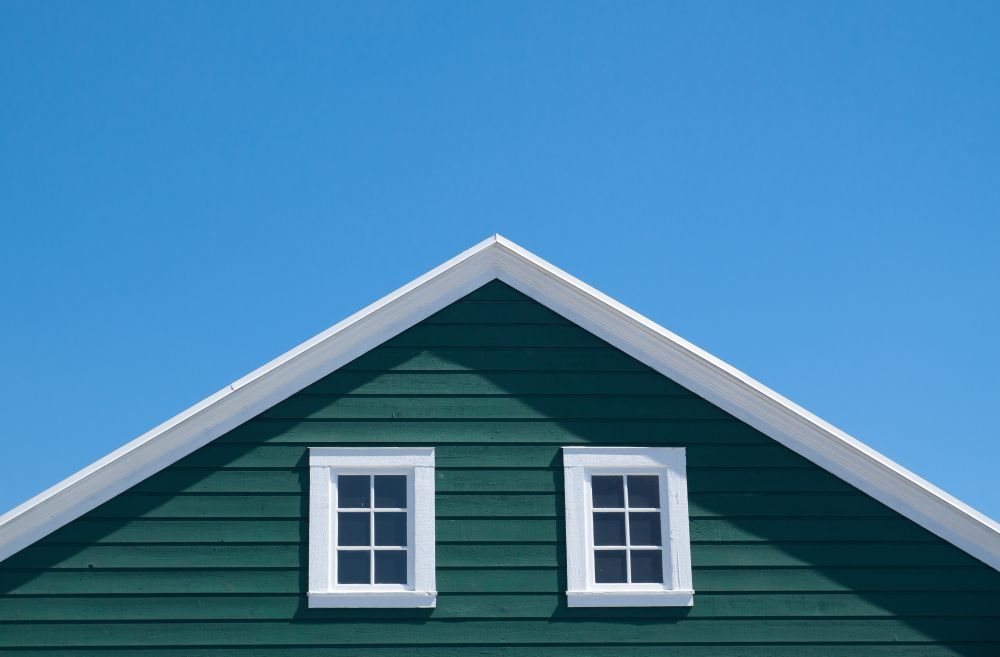 the roof of a green house with two windows against a blue sky .