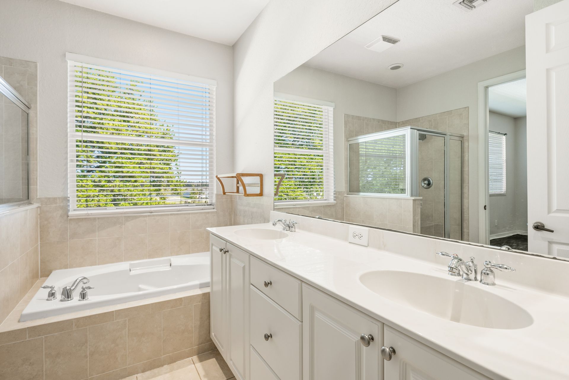 A bright, clean bathroom with white cabinetry, a single sink, a large mirror, and a soaking tub under a window.