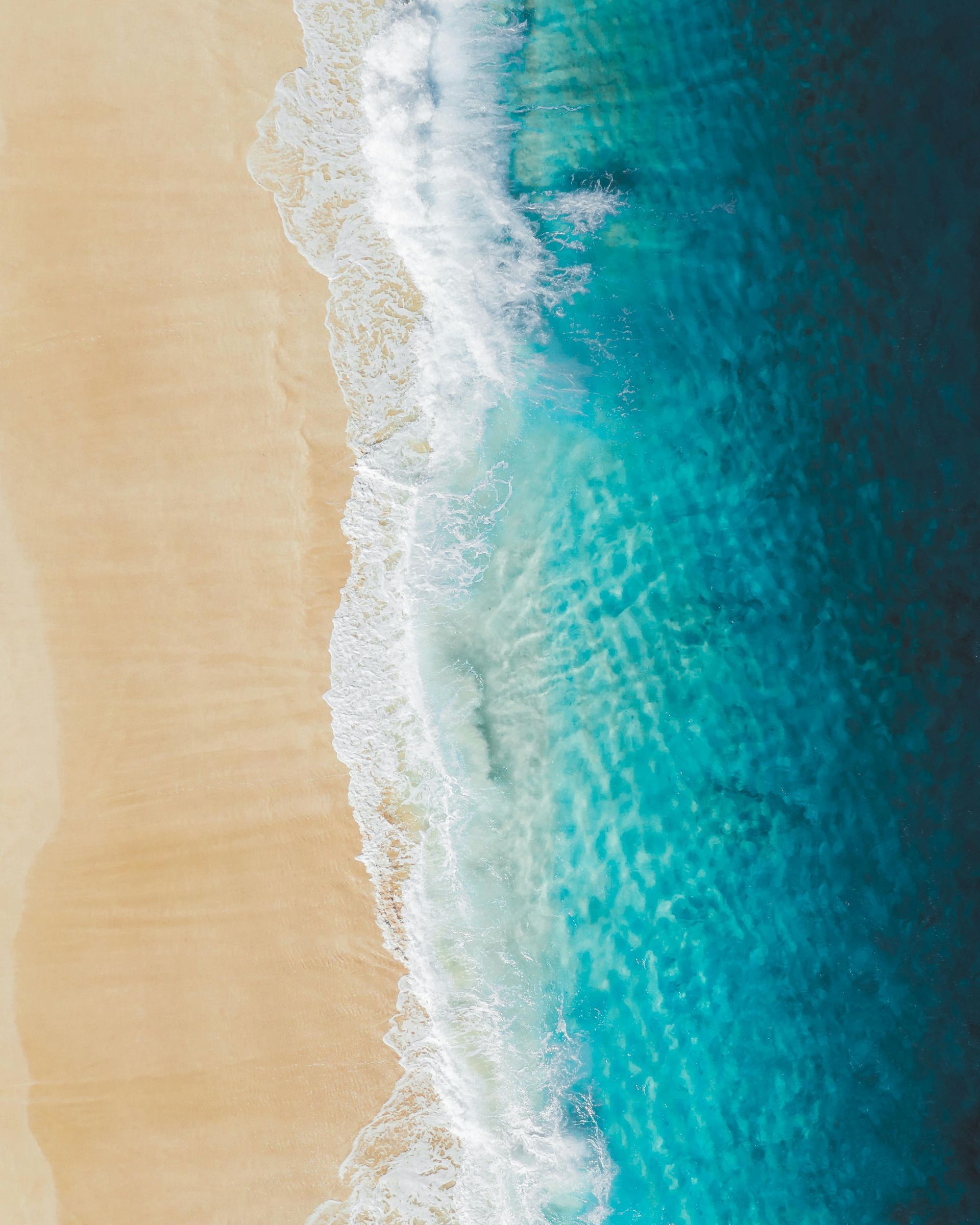 Aerial view of turquoise ocean waves gently washing over a sandy beach.