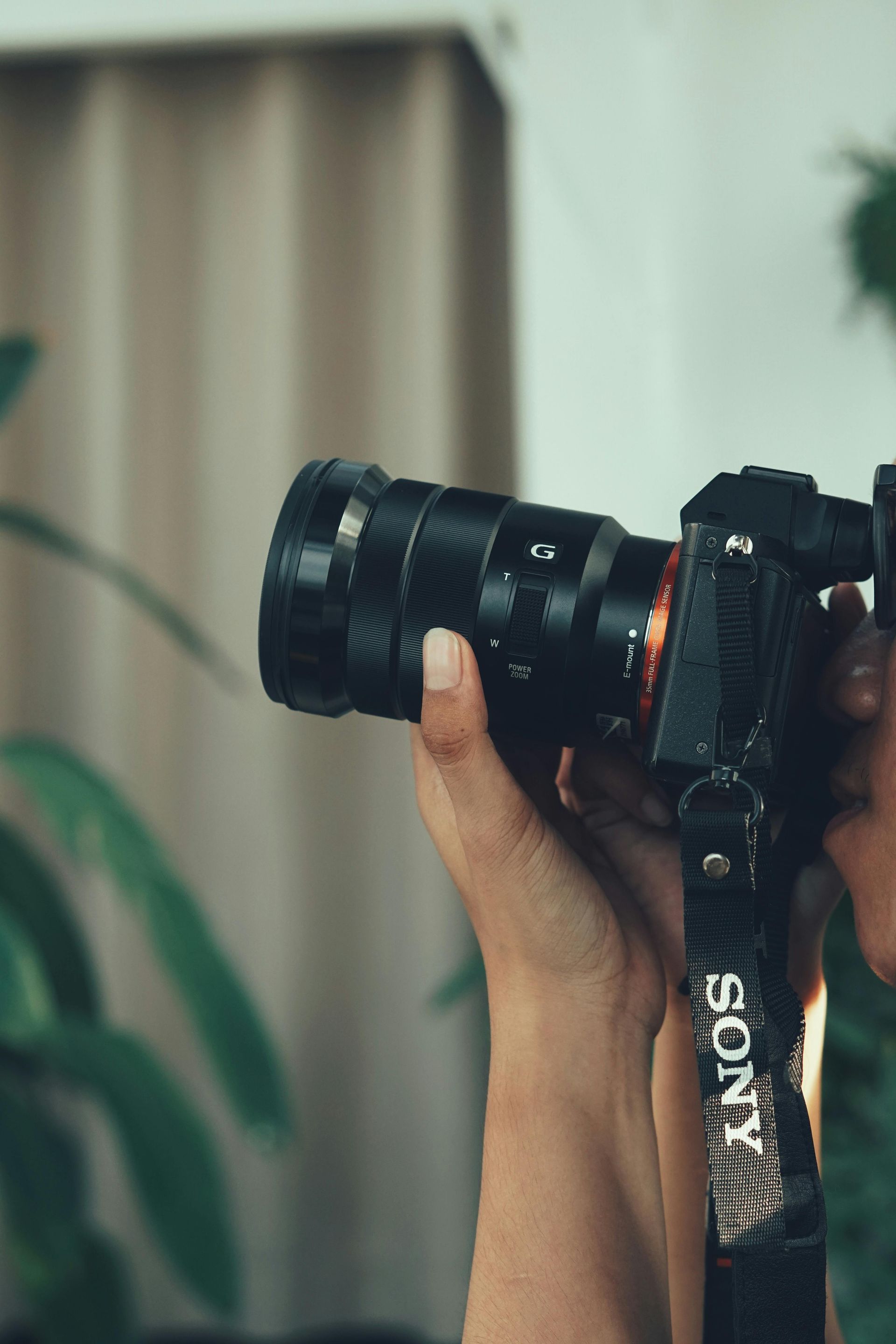 A person holds a black Sony mirrorless camera with a zoom lens, with a camera strap draped down in the foreground.