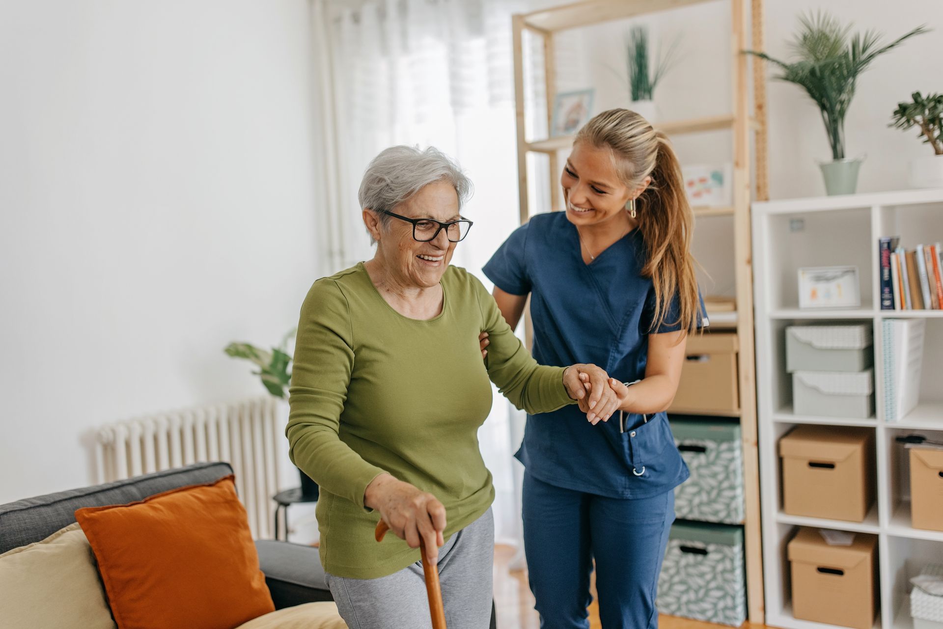 A nurse is helping an elderly woman walk in a living room.