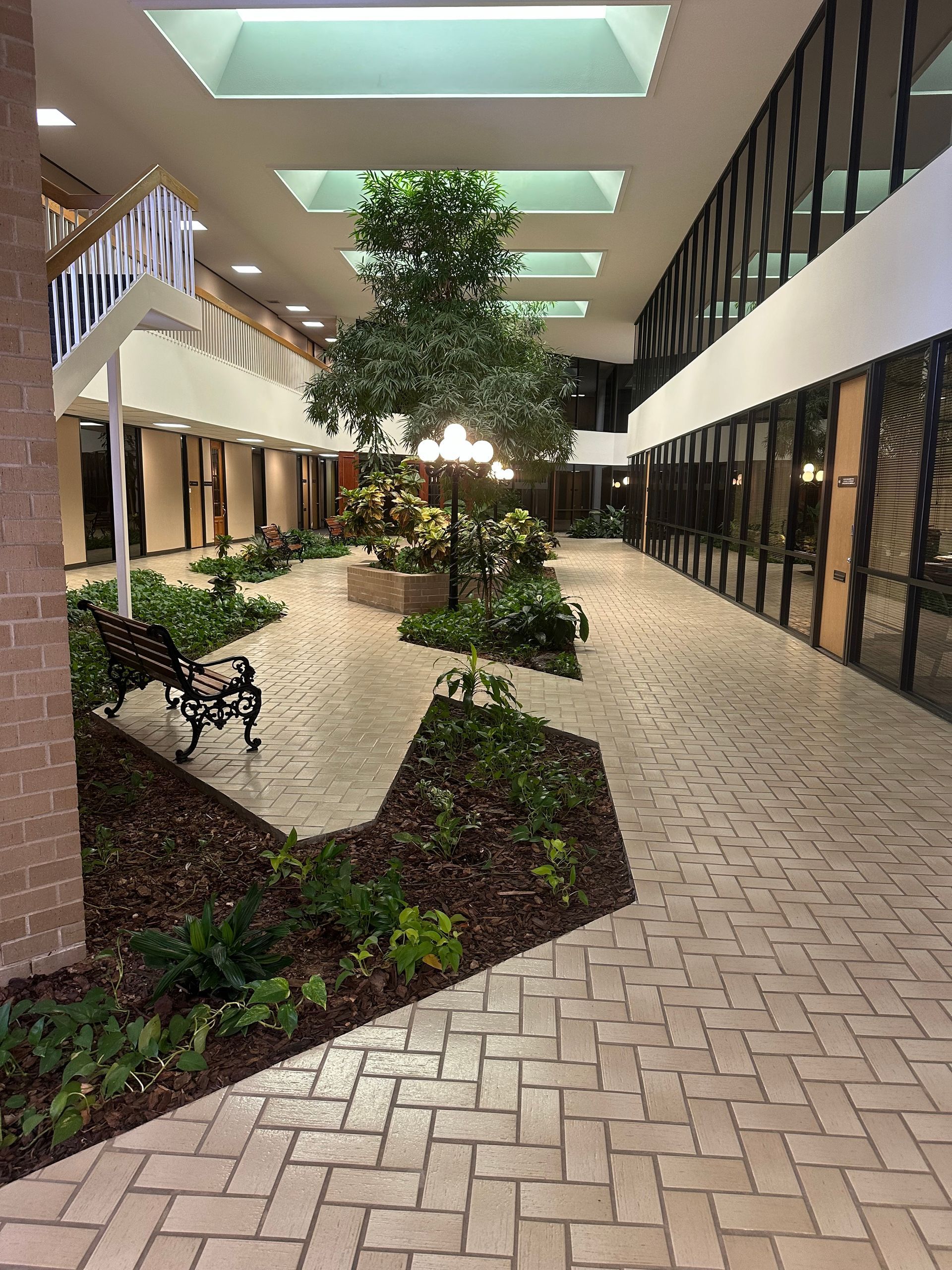 A brick walkway in a building with a bench and trees.