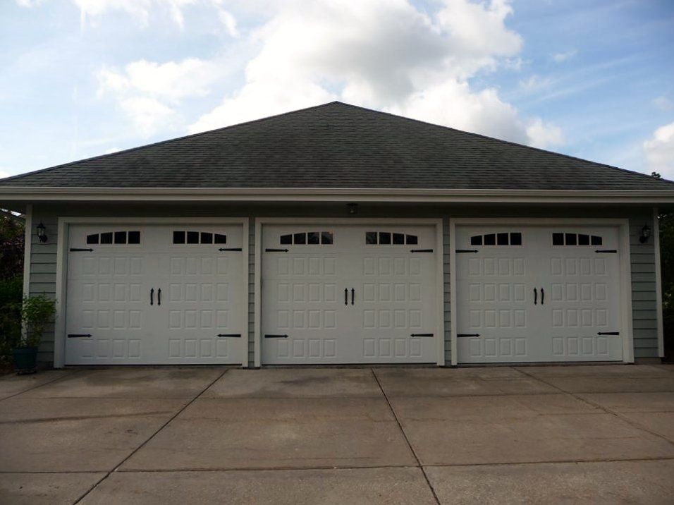 Three-car garage with white doors under a dark gray roof, set against a cloudy blue sky.