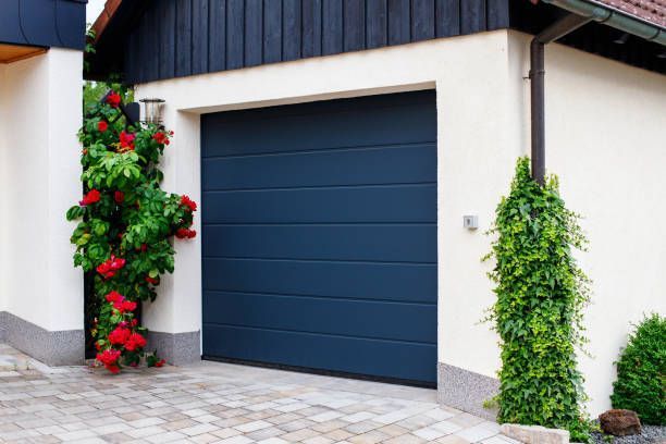 Navy blue automatic garage door near manicured blooming roses.