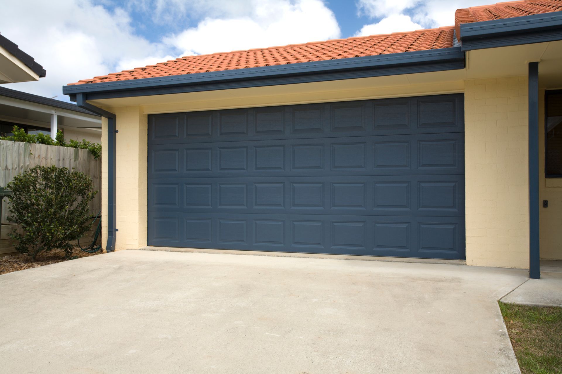 Blue garage door on beige house with red roof and concrete driveway.