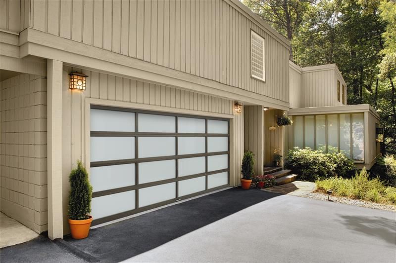 Modern house with garage; tan siding, frosted glass garage door, black asphalt driveway.