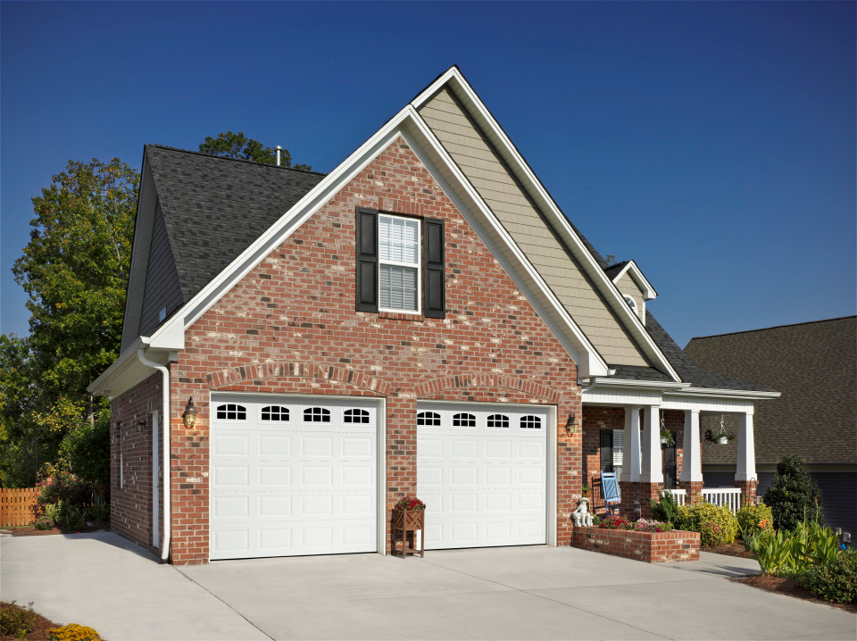 Brick house with white garage doors, under a blue sky.