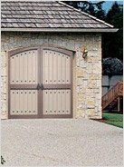 Tan stone garage with a wooden double door with decorative studs. A driveway and a small section of a wooden staircase.