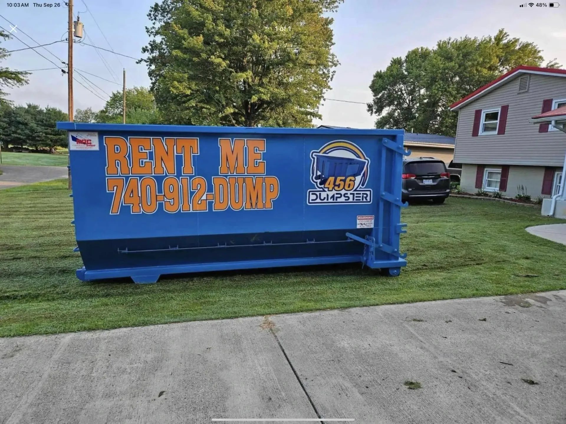A dumpster is sitting in a gravel lot next to a truck.