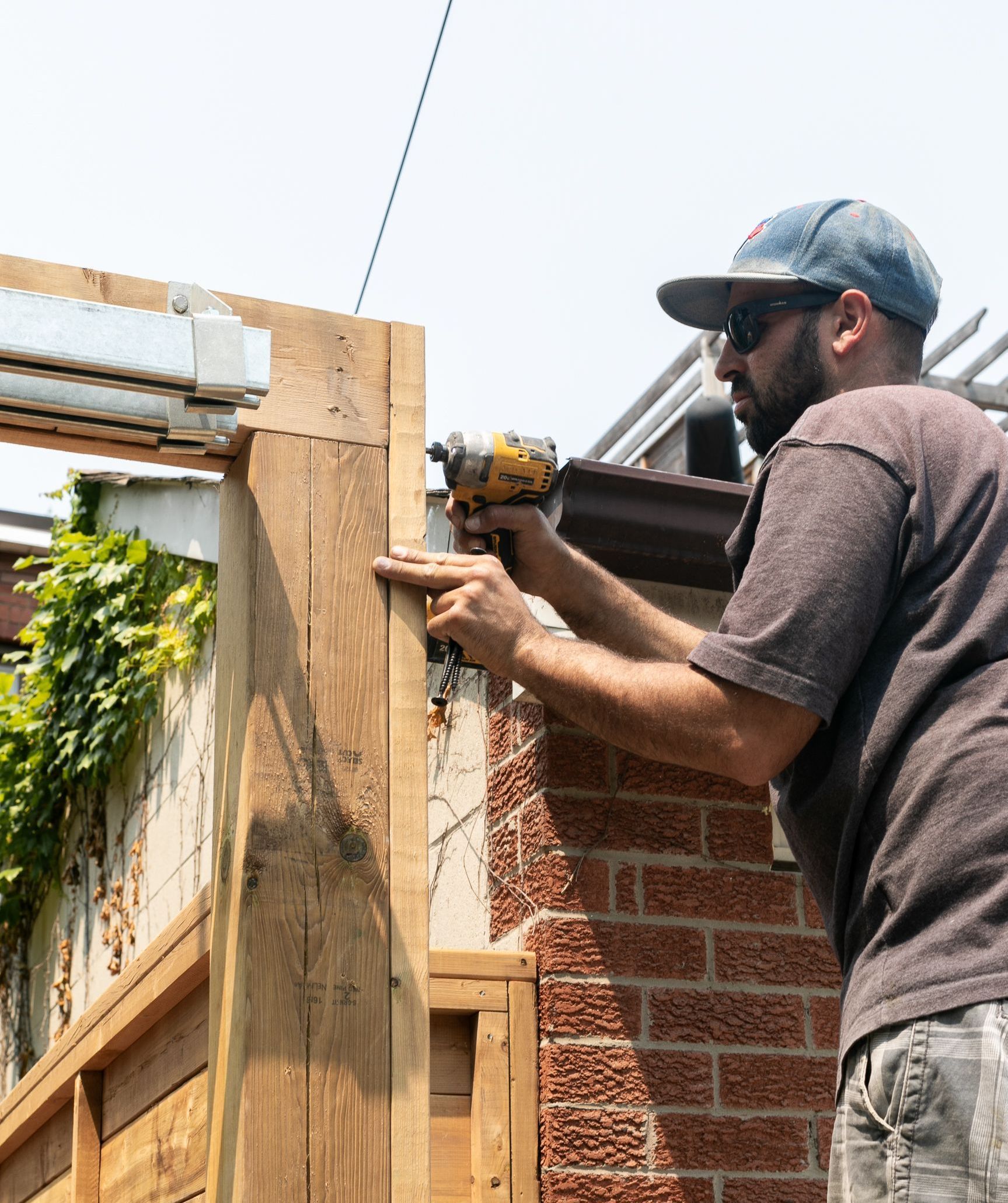 A man is working on a wooden fence with a drill.