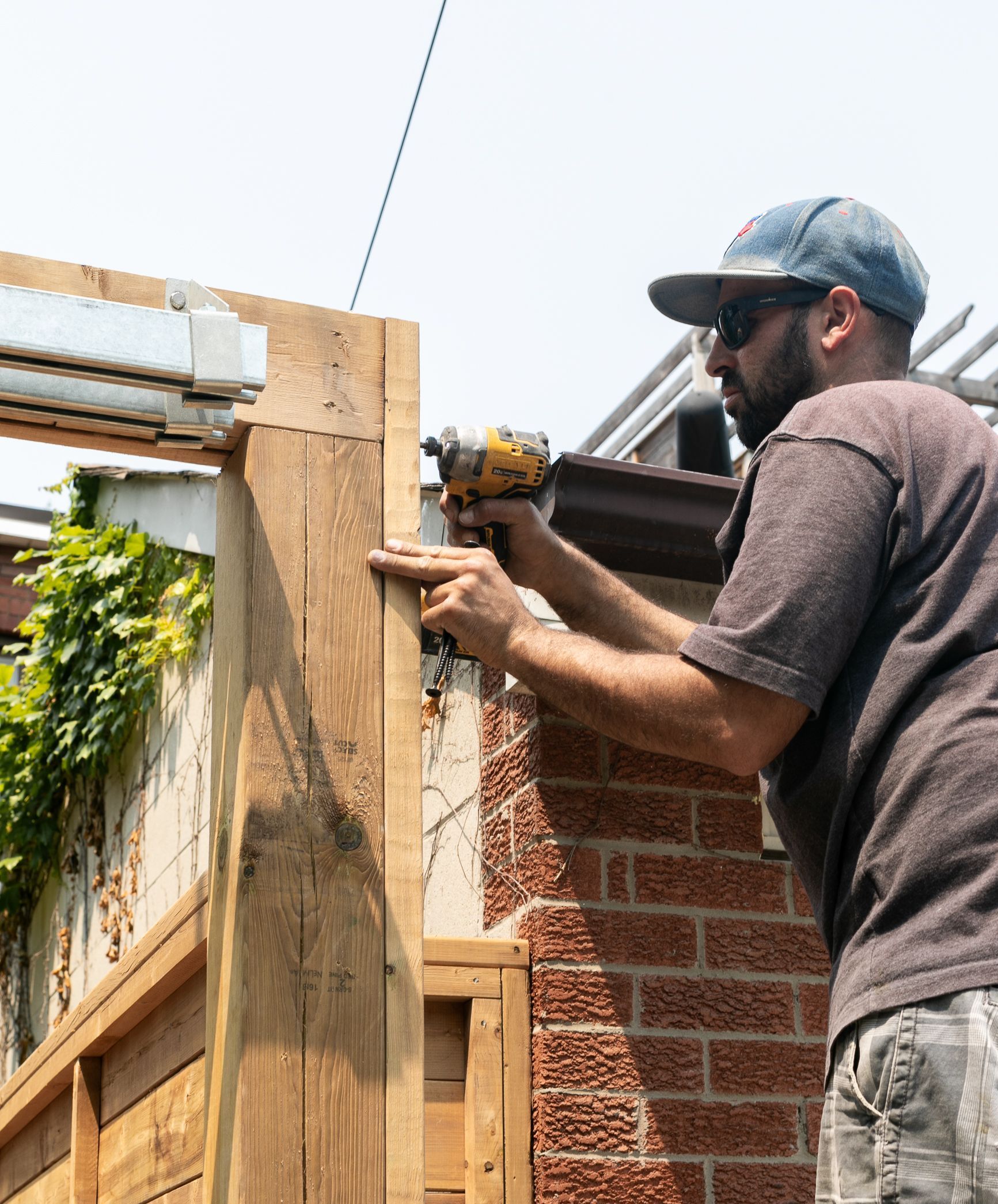 A man is working on a wooden fence with a drill.