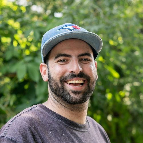 A man with a beard is wearing a blue jays hat and smiling.