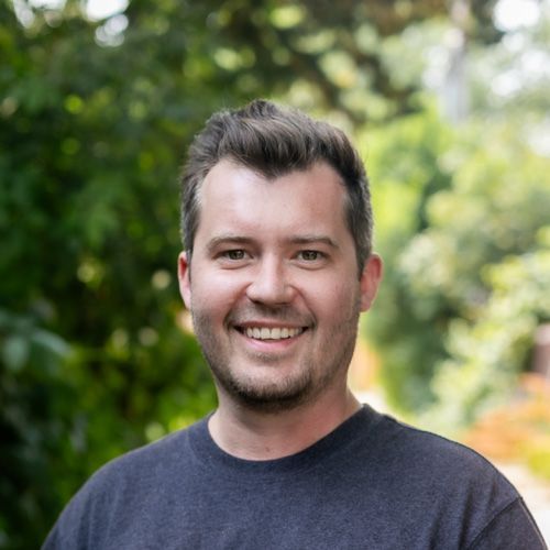 A man with a beard is smiling for the camera while wearing a black shirt.