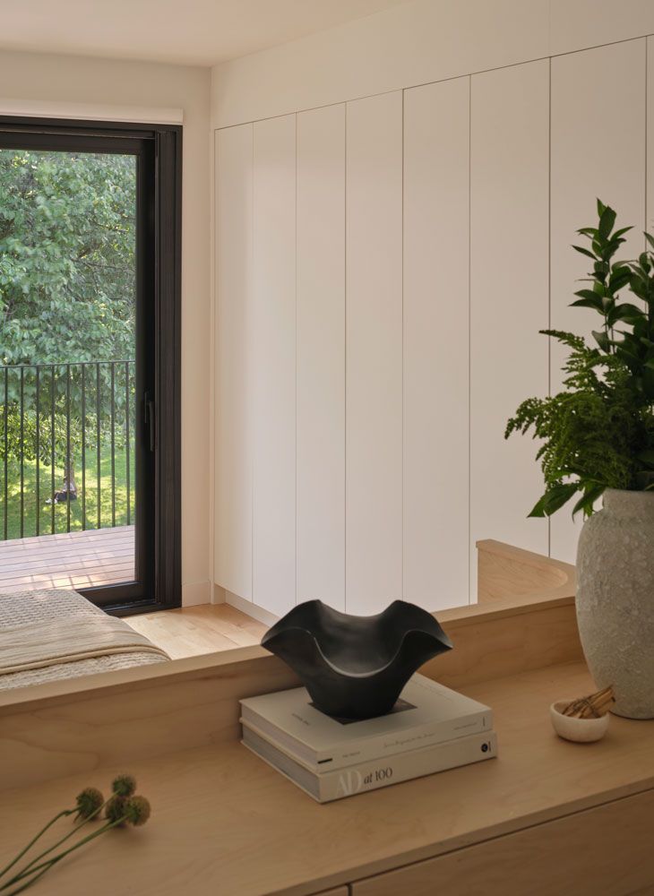 A modern interior with a wooden counter, black bowl, greenery, and a view of trees through a window.