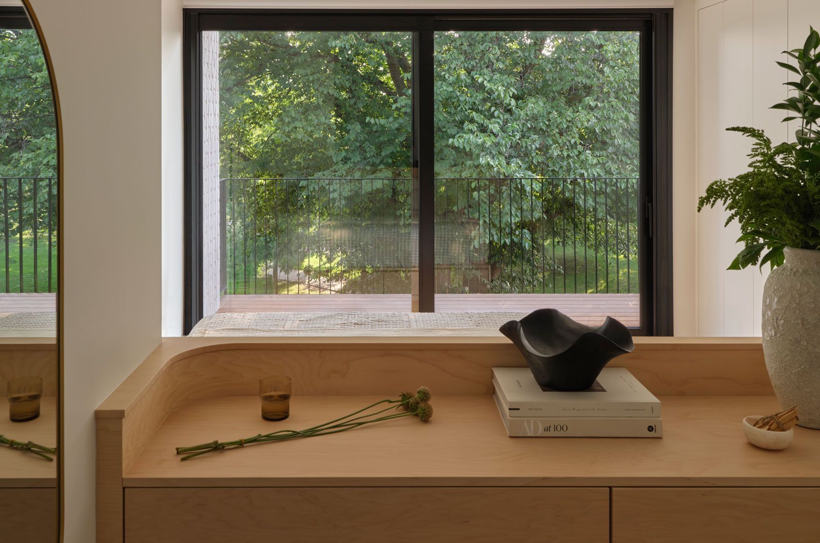 A modern two-story house with a flat black roof and a balcony nestled among green trees.
