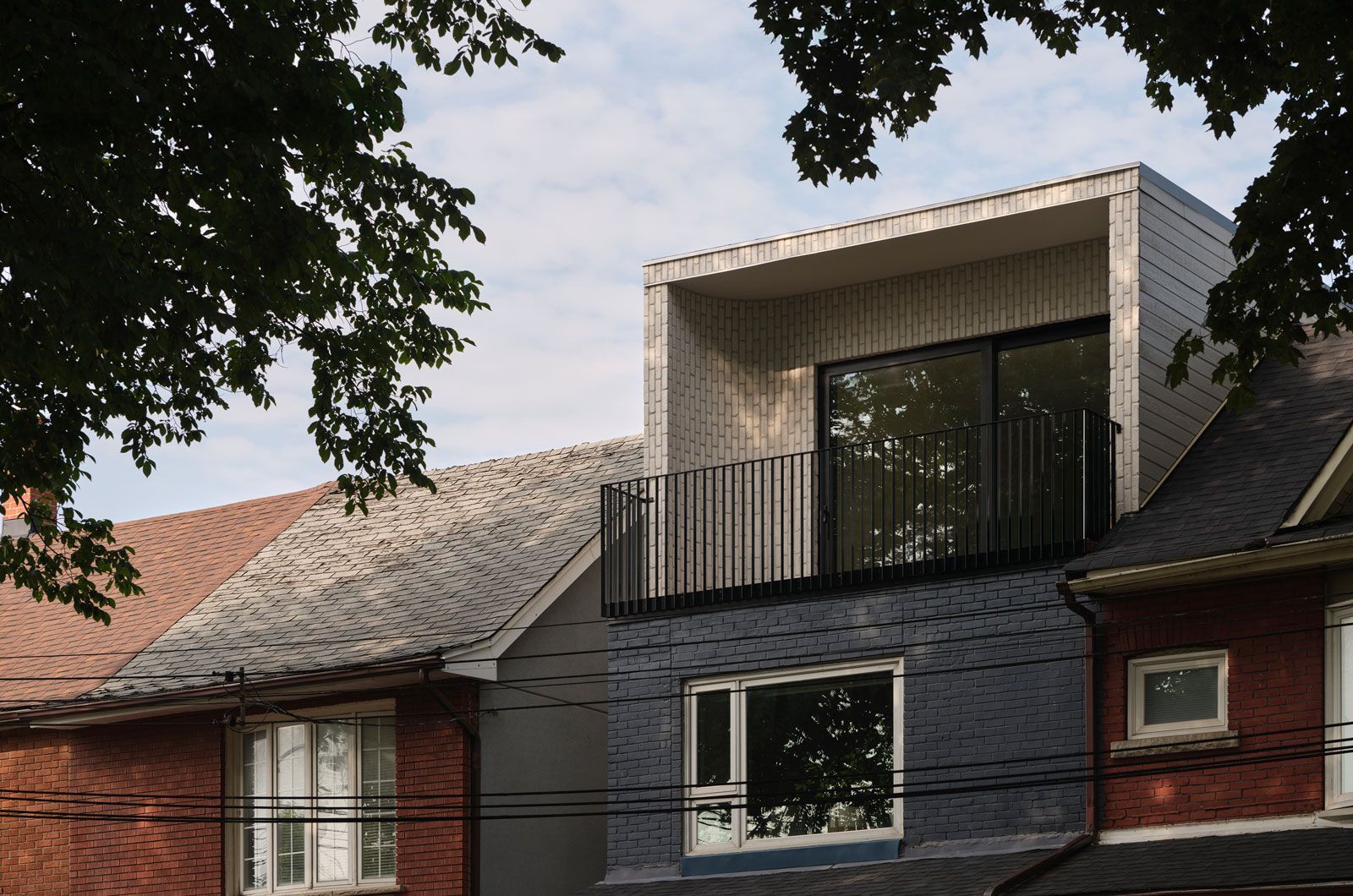 Modern two-story home exterior, gray siding, flat-roofed extension with balcony, framed by trees.