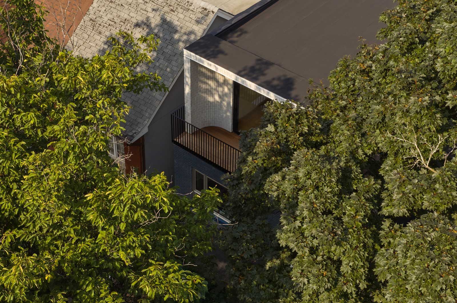A modern two-story house with a flat black roof and a balcony nestled among green trees.
