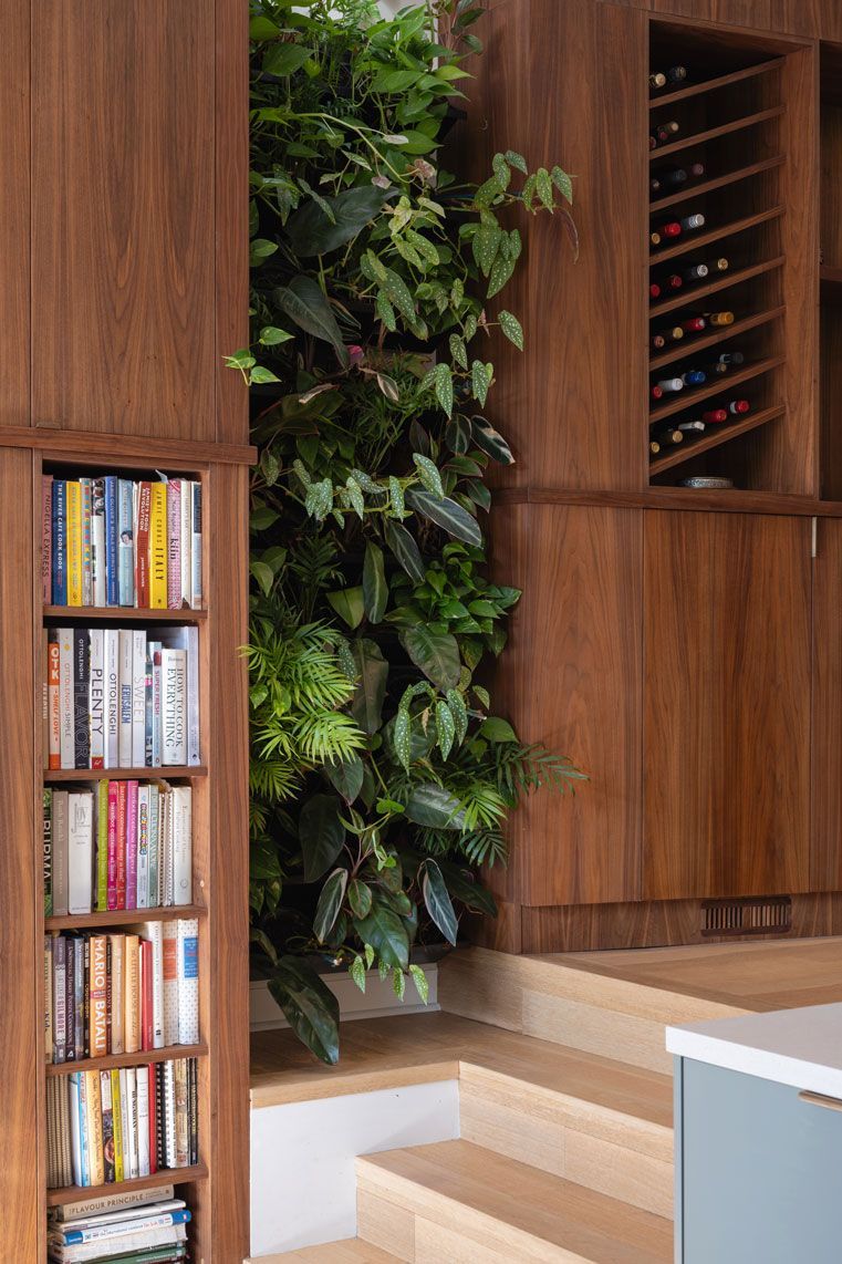 A bookshelf with books on it next to a wall with plants growing on it.
